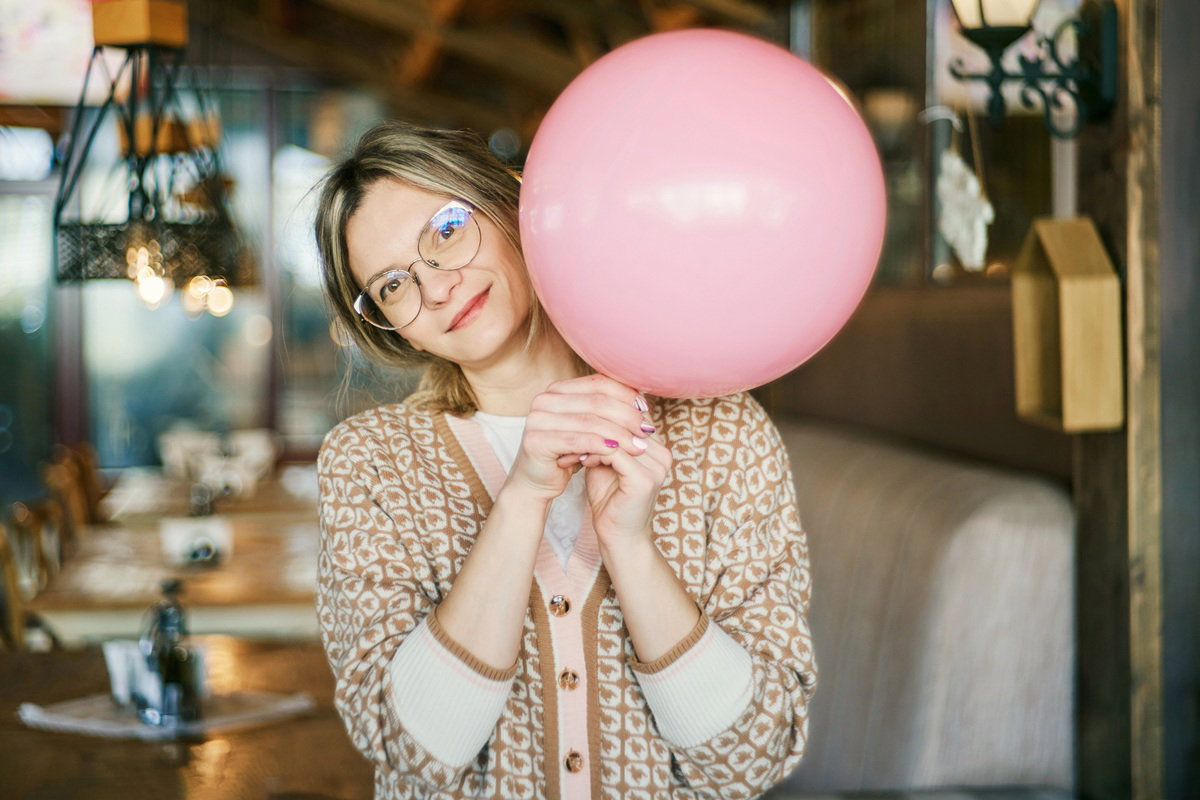 kobieta w wieku 35 plus w okularach stoi z balonikiem i uśmiecha się