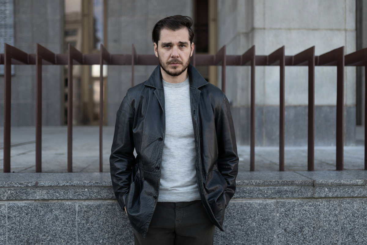 mężczyzna w wieku około 40 lat w kurtce i ze smutną twarzą stoi na tle budynku