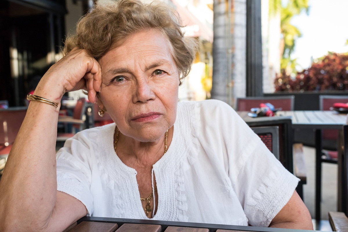 kobieta w wieku 65 plus w białej bluzce siedzi zamyślona na tarasie