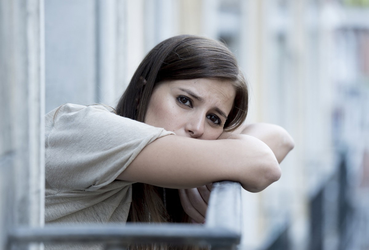 młoda kobieta 30 plus stoi na balkonie załamana opiera się o balustradę