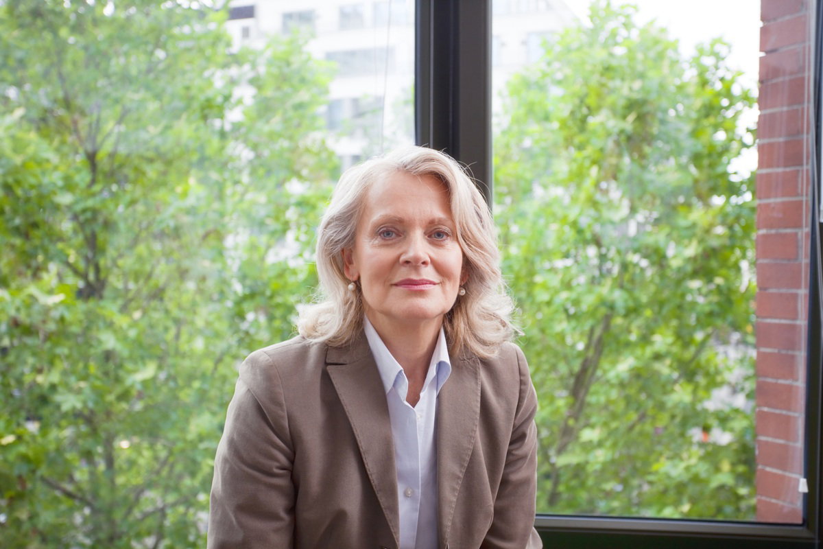 kobieta w wieku około 50 plus blondynka siedzi poważna zamyślona na tle okna i drzew