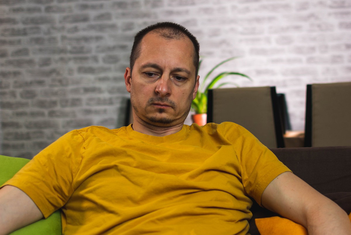 mężczyzna w wieku 40 plus w złotym t-shircie siedzi na kanapie załamany