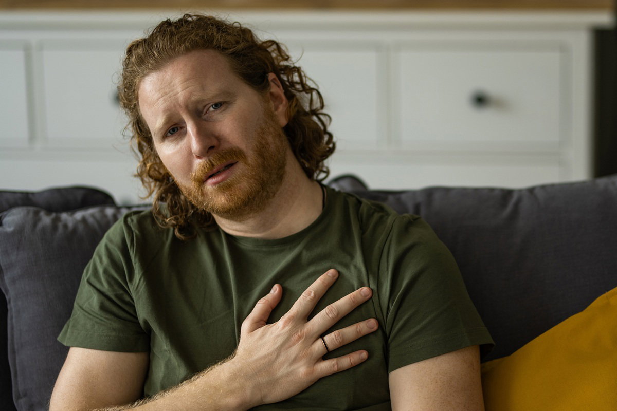 mężczyzna w wieku 35 plus z rudymi kręconymi włosami siedzi na kanapie i jest załamany