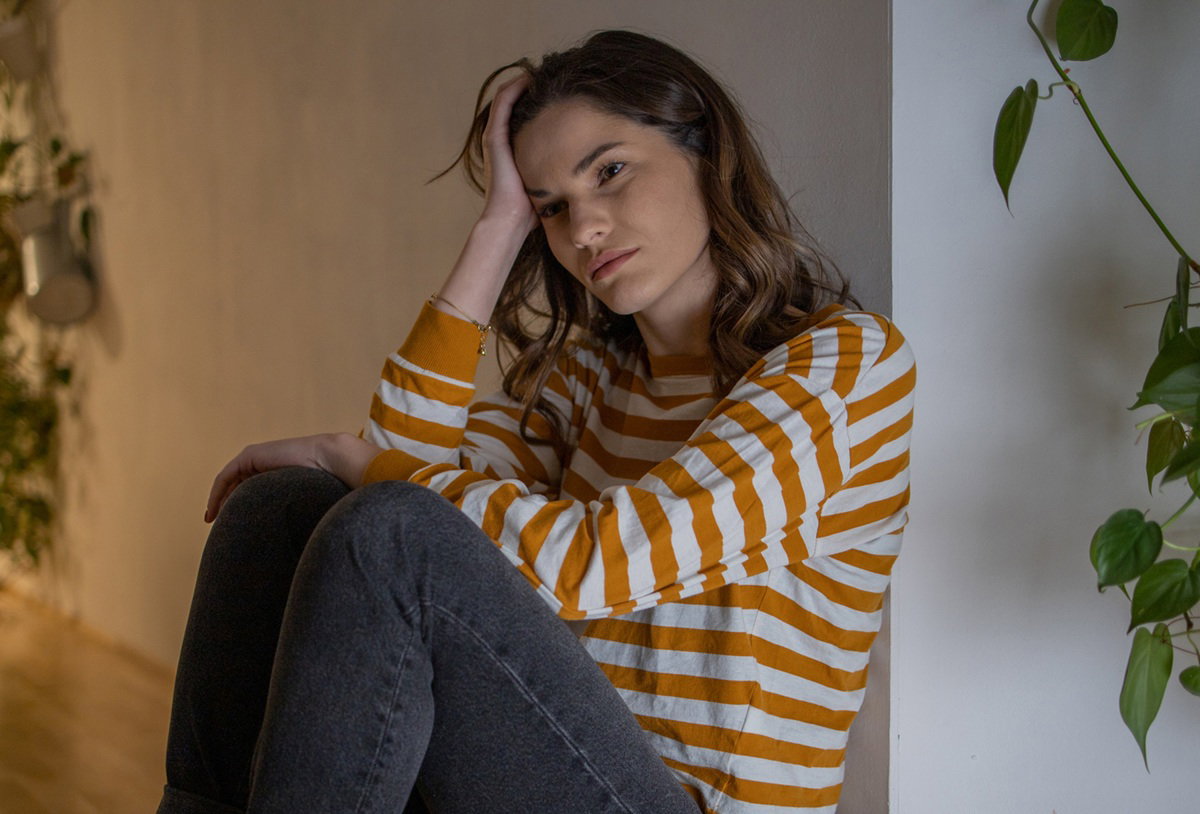 kobieta w wieku około 30 lat w bluzce w paski siedzi na podłodze załamana