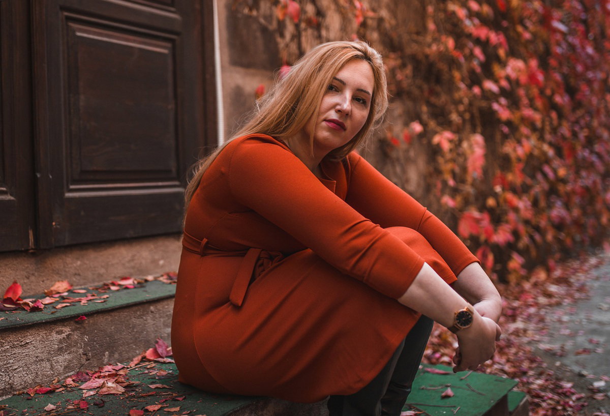 smutna kobieta w wieku około 30 lat w czerwonej sukience siedzi na tle drzwi na schodach