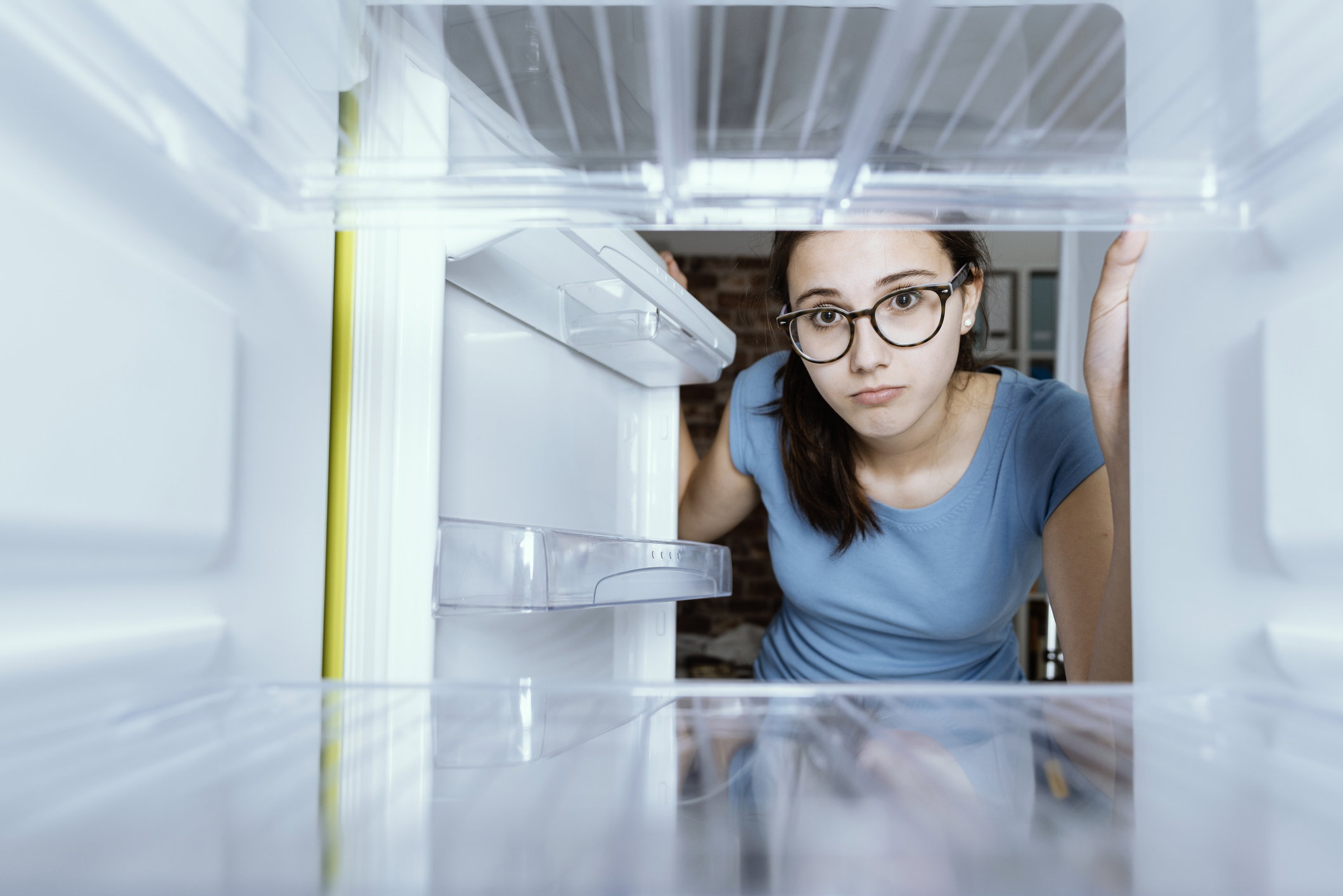 Sad woman looking into her empty fridge with no groceries