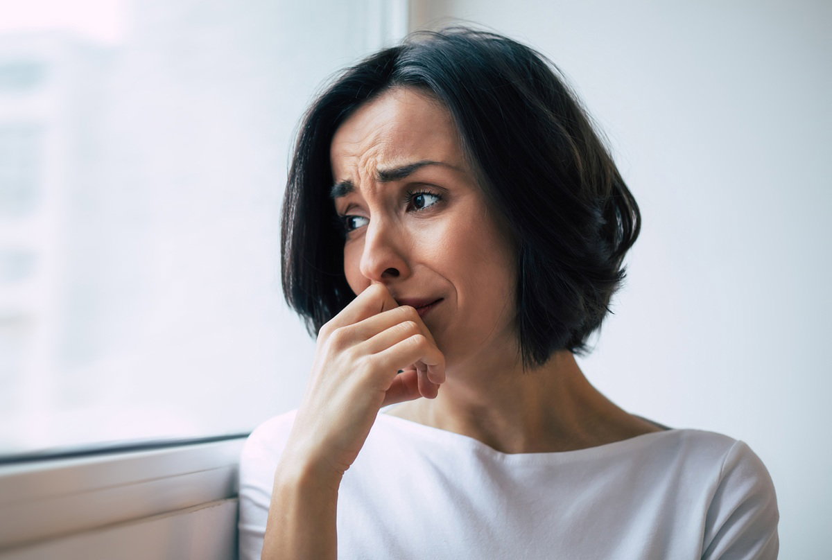 kobieta w wieku około 35 plus w białej bluzce siedzi w zmartwiona i patrzy przez okno