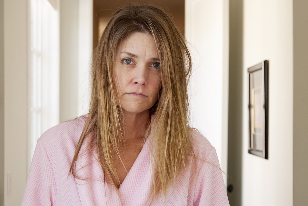 kobieta w wieku 40 plus z długimi włosami w różowym szlafroku stoi w korytarzu załamana