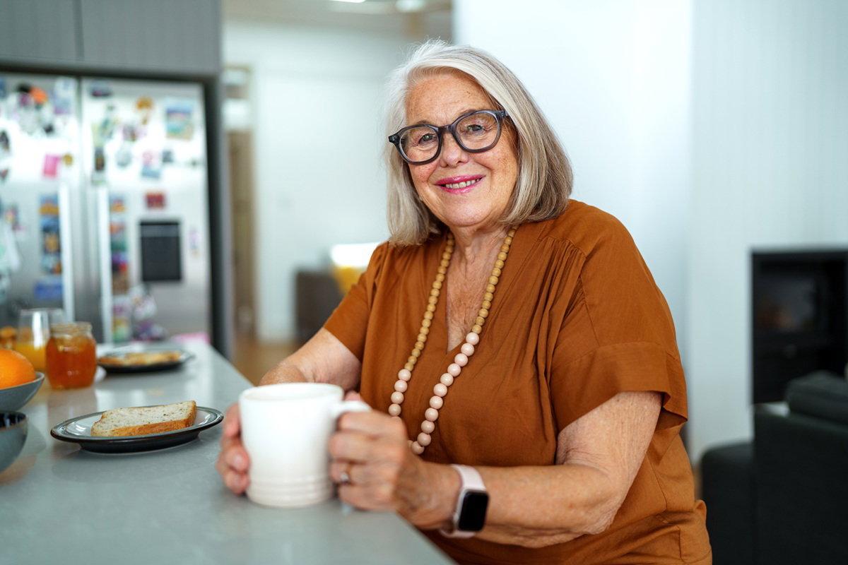 kobieta w wieku około 70 lat w okularach i z koralami na szyi siedzi w kuchni i się uśmiecha