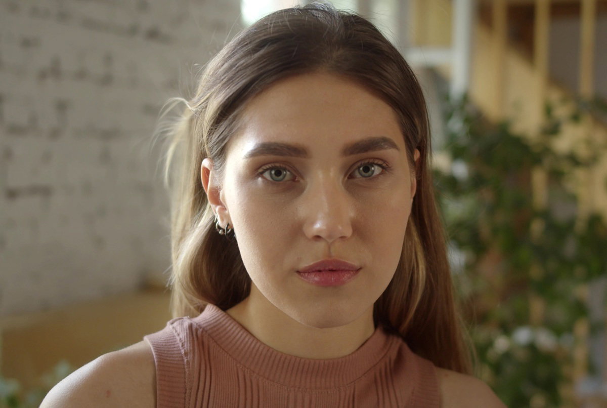 młoda dziewczyna lat około 20 siedzi w salonie na tle schodów zamyślona