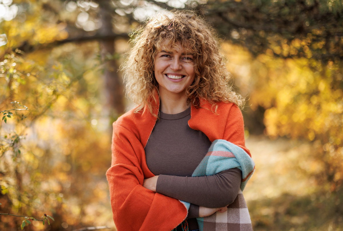 kobieta w wieku 30 plus na spacerze w jesiennym lesie okryta kocem i uśmiechnięta