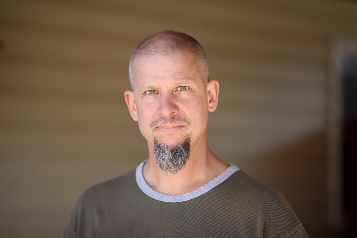 mężczyzna w wieku 45 plus z wąsami i kozią bródką patrzy zamyślony przed siebie