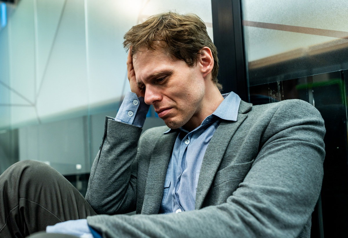 mężczyzna w wieku około 35 lat siedzi zrozpaczony na ziemi w biurze