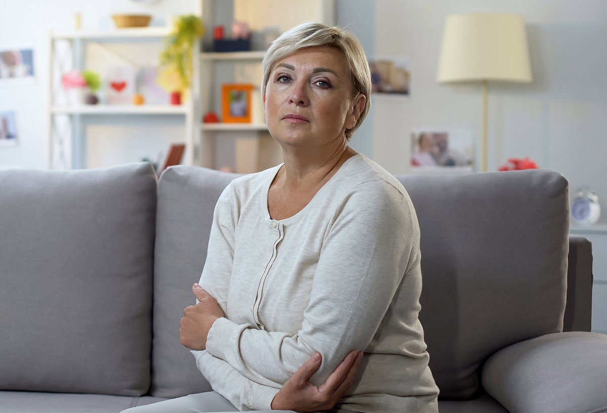 kobieta w wieku około 50 lat z krótkimi blond włosami siedzi na kanapie zmartwiona