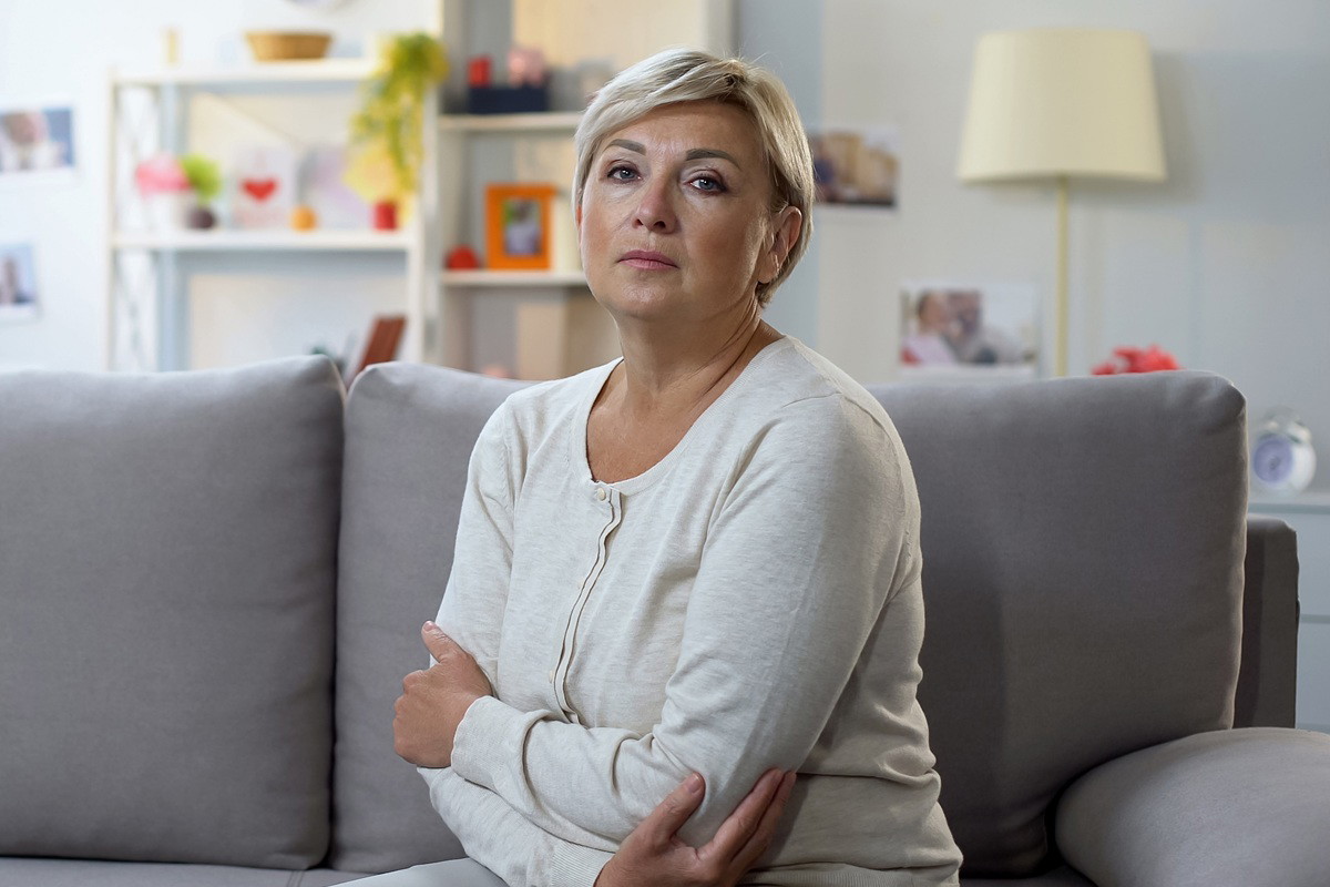 kobieta w wieku około 50 lat z krótkimi blond włosami siedzi na kanapie zmartwiona