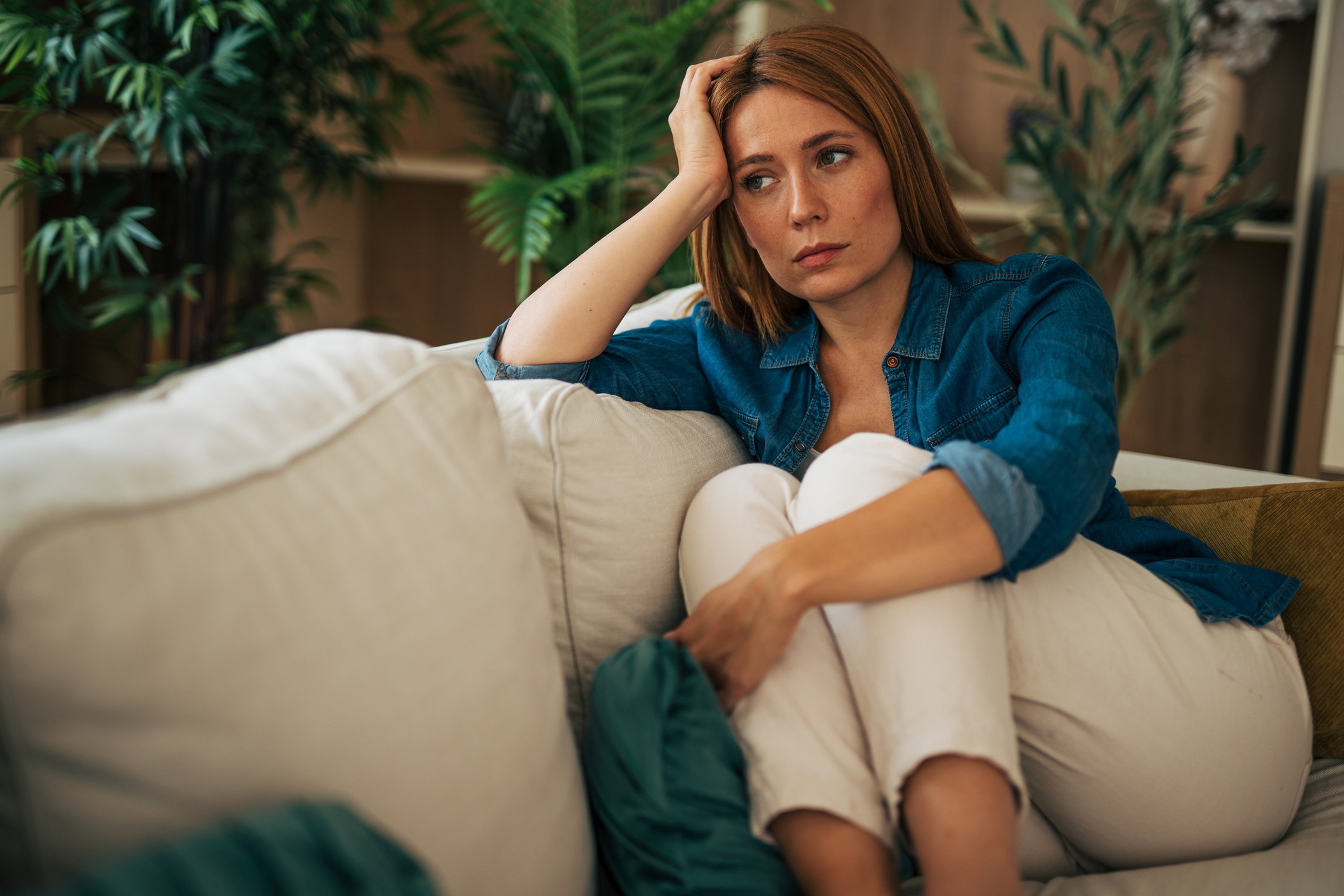 Sad young woman sitting on sofa at home feeling depressed
