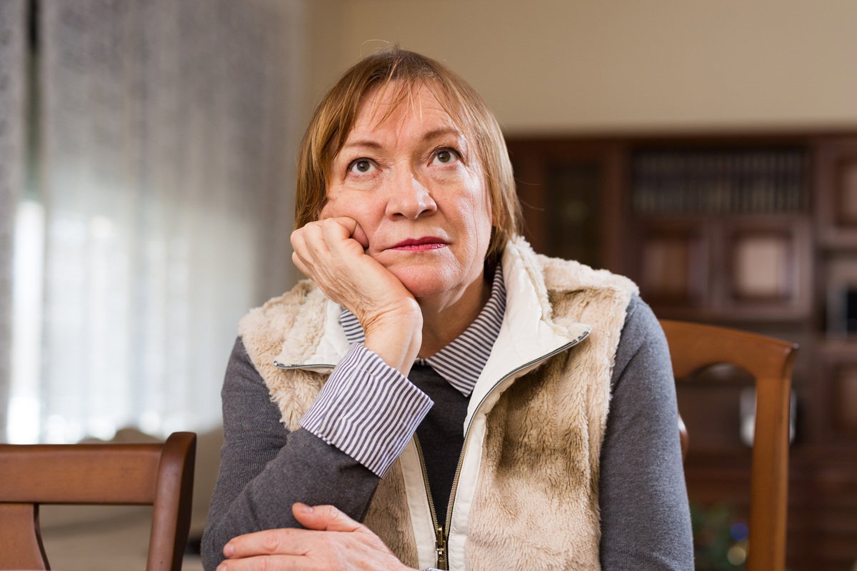 kobieta w wieku 65 plus ciepło ubrana siedzi i rozmyśla w salonie przy stole