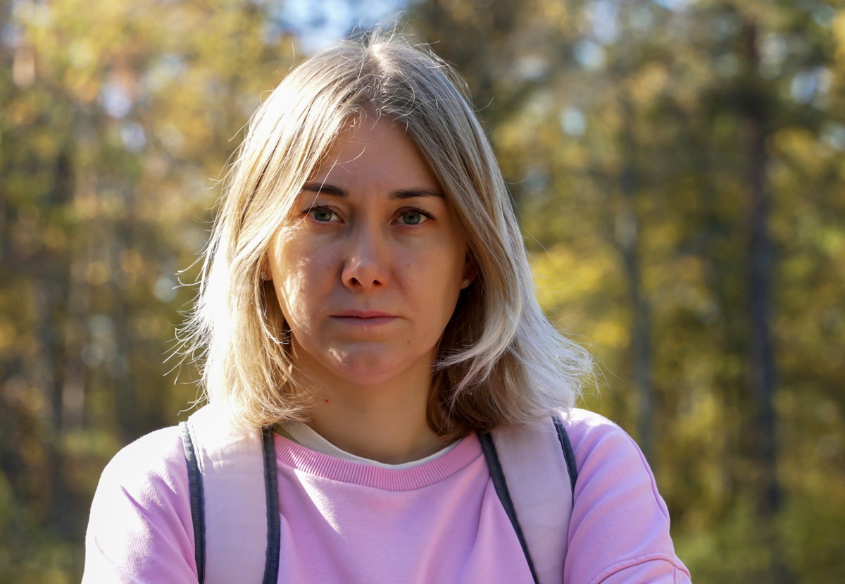 kobieta w wieku około 40 lat blondynka w różowej bluzie stoi na tle jesiennych drzew w parku smutna