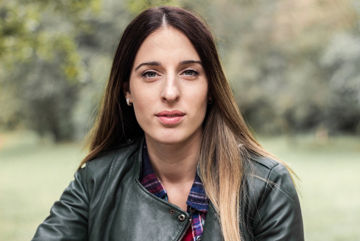 młoda kobieta w wieku 25 plus z długimi włosami w skórzanej kurtce siedzi na zewnątrz lekko smutna