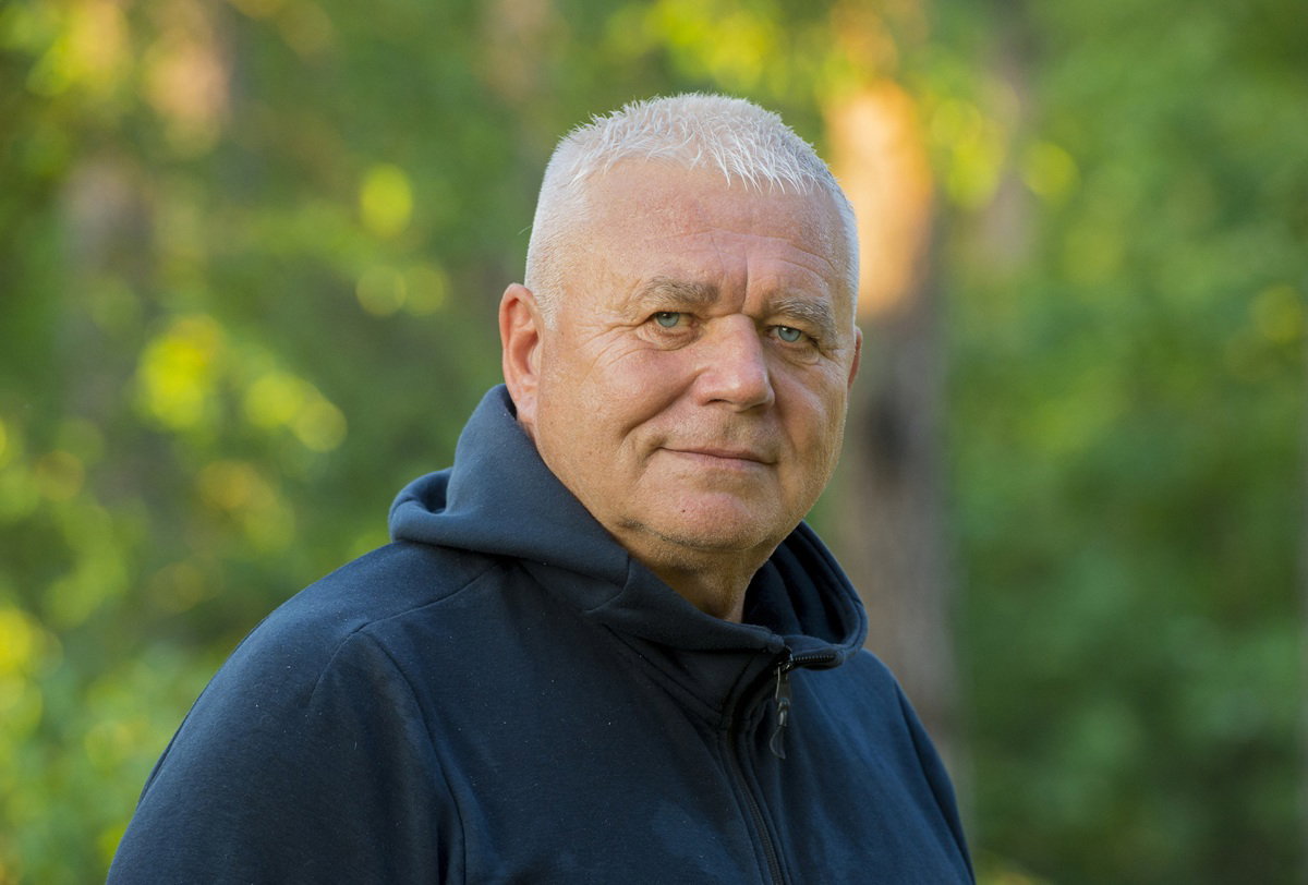 mężczyzna w wieku około 65 plus w bluzie z kapturem stoi na zewnątrz z poważnym spojrzeniem