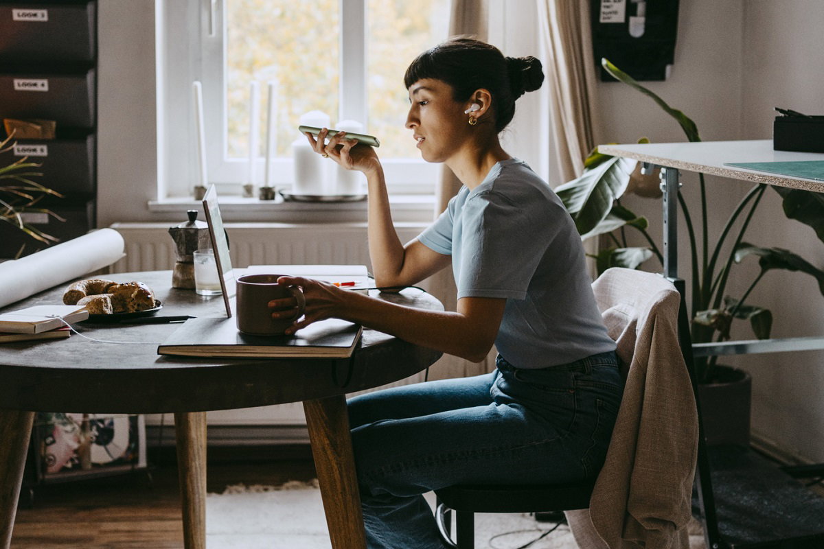 Side view of female freelancer talking on speaker while sitting on chair at home office