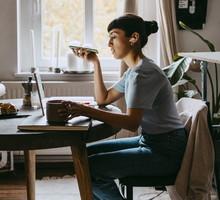 Side view of female freelancer talking on speaker while sitting on chair at home office