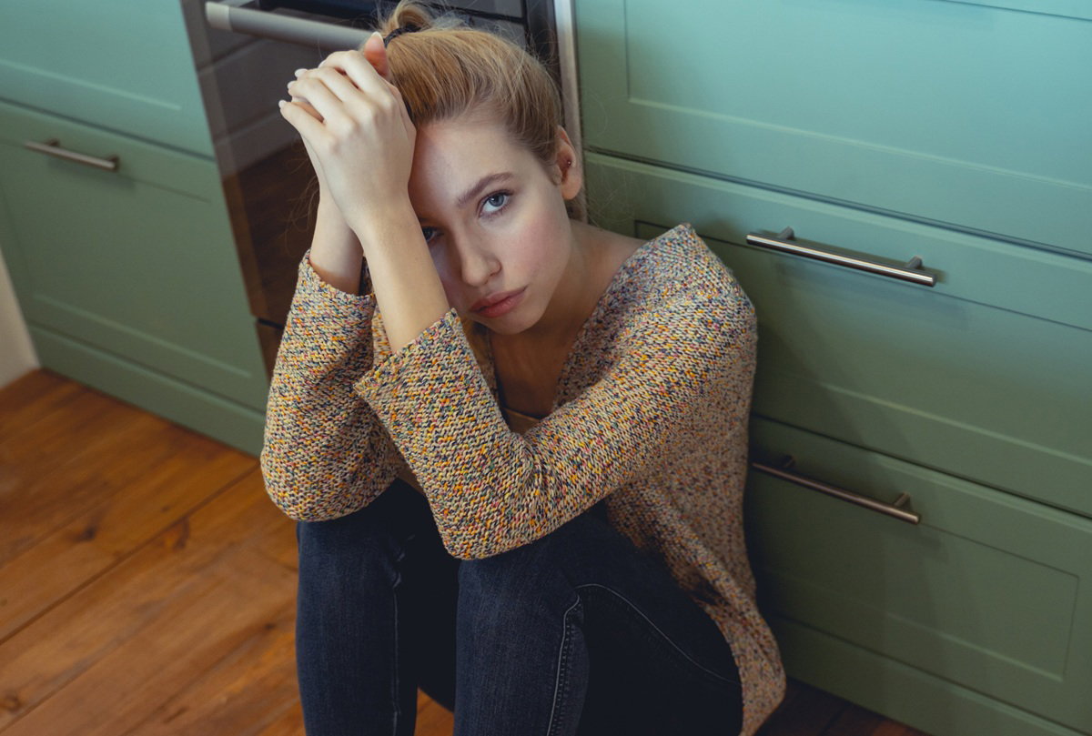 młoda kobieta około 30 lat siedzi na podłodze w kuchni zrozpaczona