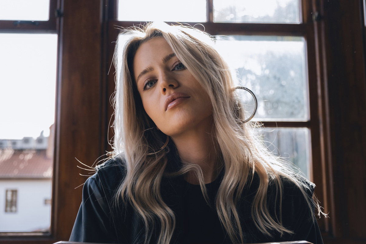 kobieta w wieku 30 plus blondynka siedzi na tle okna i patrzy z dumą i pogardą