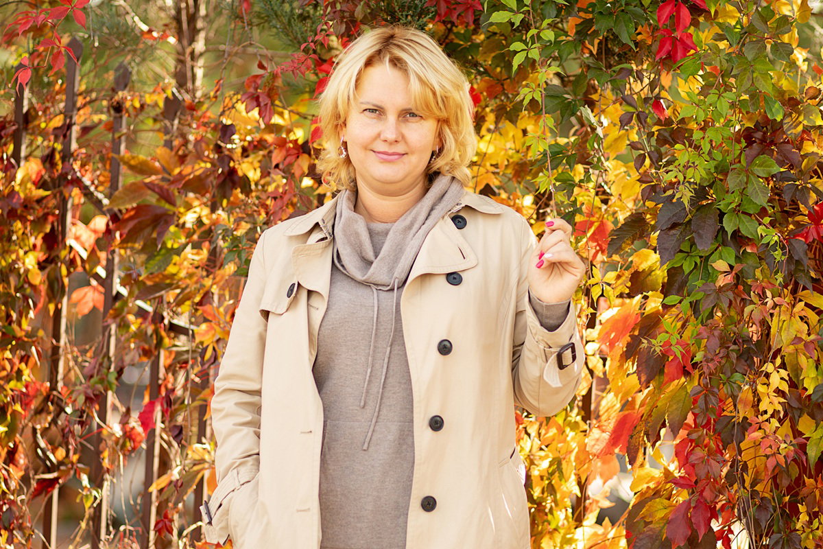 kobieta  w wieku 30 plus blondynka stoi na tle kolorowych jesiennych liści i lekko się uśmiecha