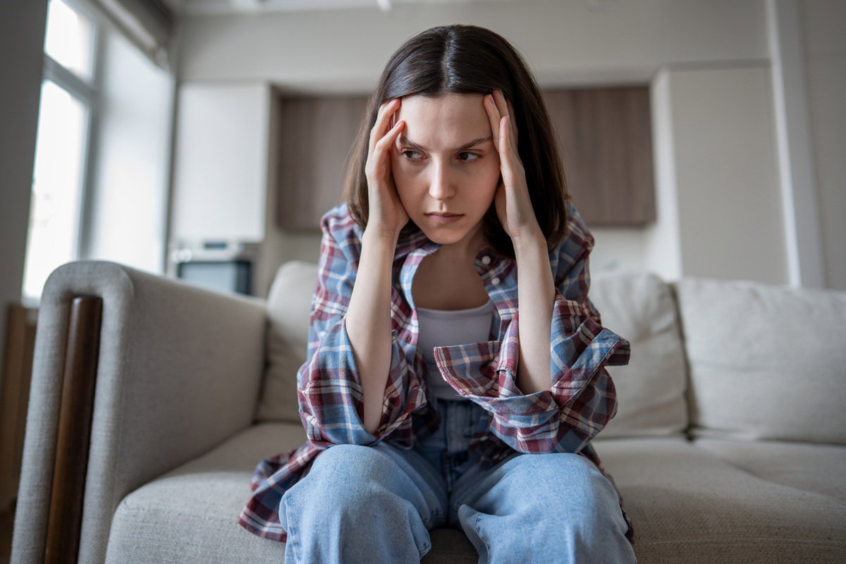 kobieta w wieku 30 plus w koszuli w kratę siedzi na kanapie załamana i wściekła