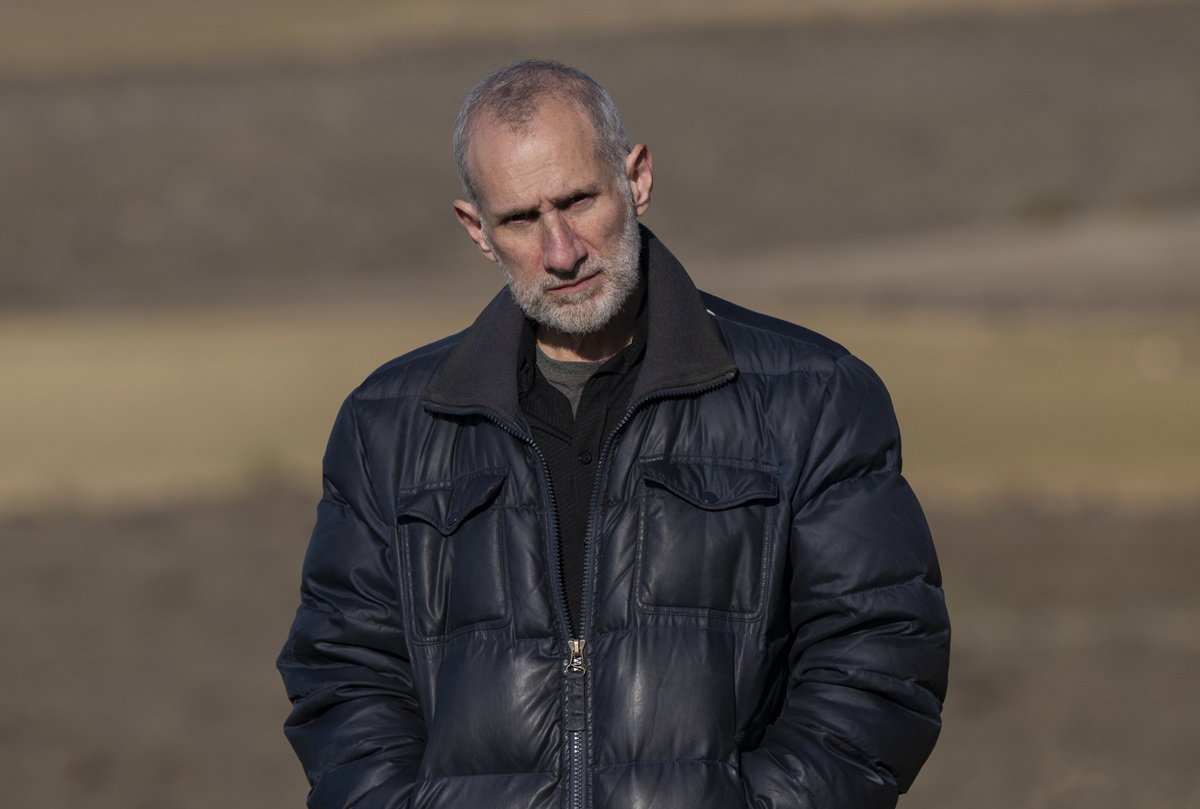 mężczyzna w wieku 50 plus w czarnej kurtce stoi na polu zasępiony i zgorzkniały