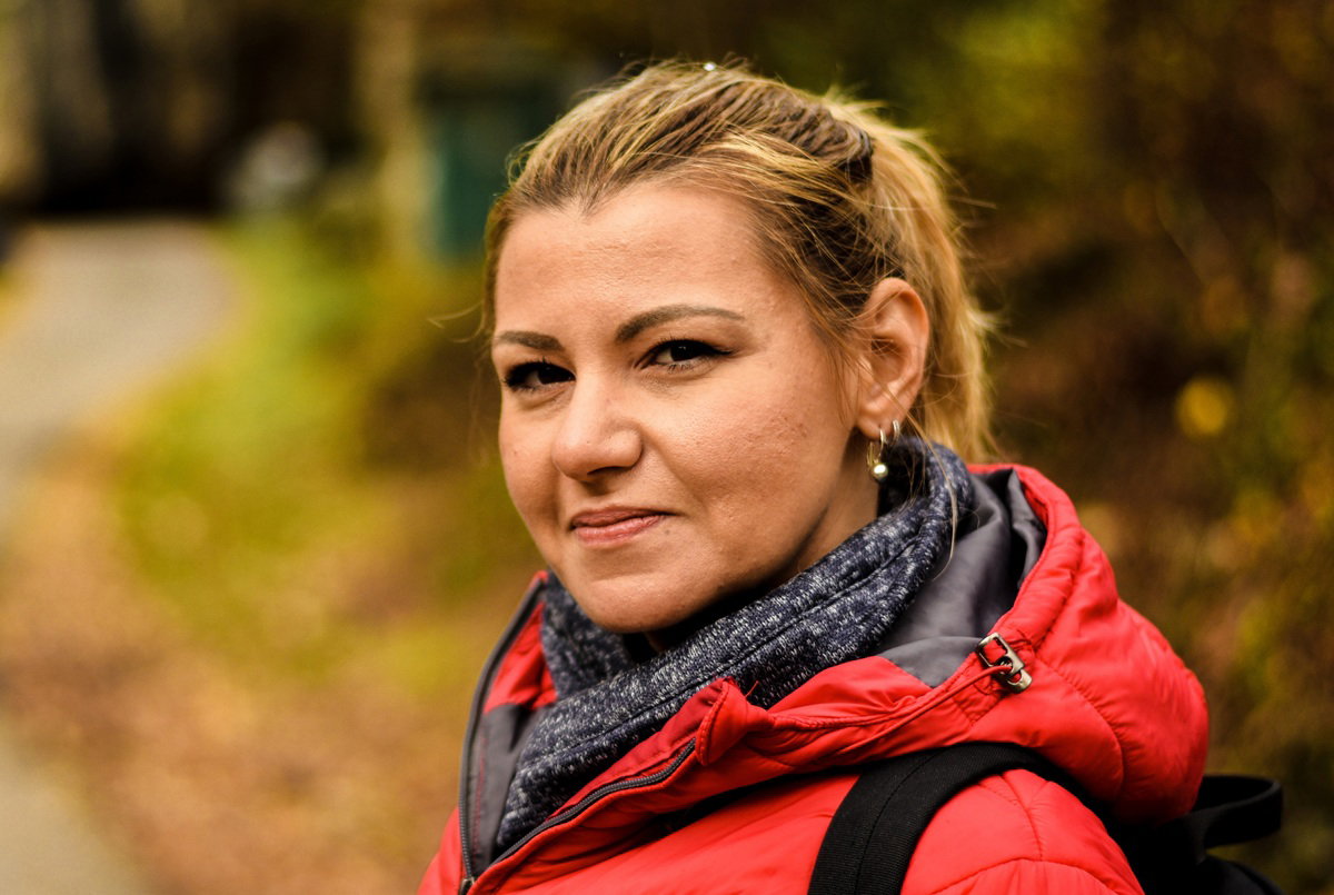 kobieta w wieku 35 plus w czerwonej kurtce blondynka stoi na zewnątrz i delikatnie się uśmiecha