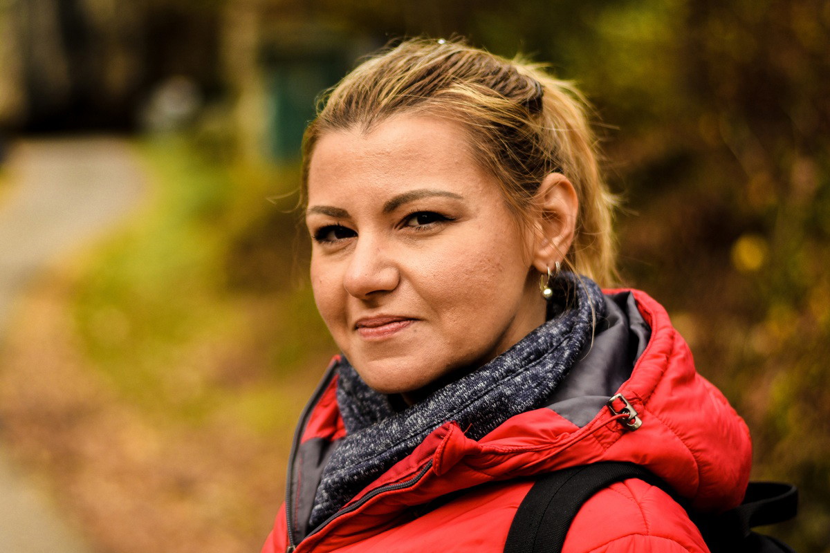 kobieta w wieku 35 plus w czerwonej kurtce blondynka stoi na zewnątrz i delikatnie się uśmiecha