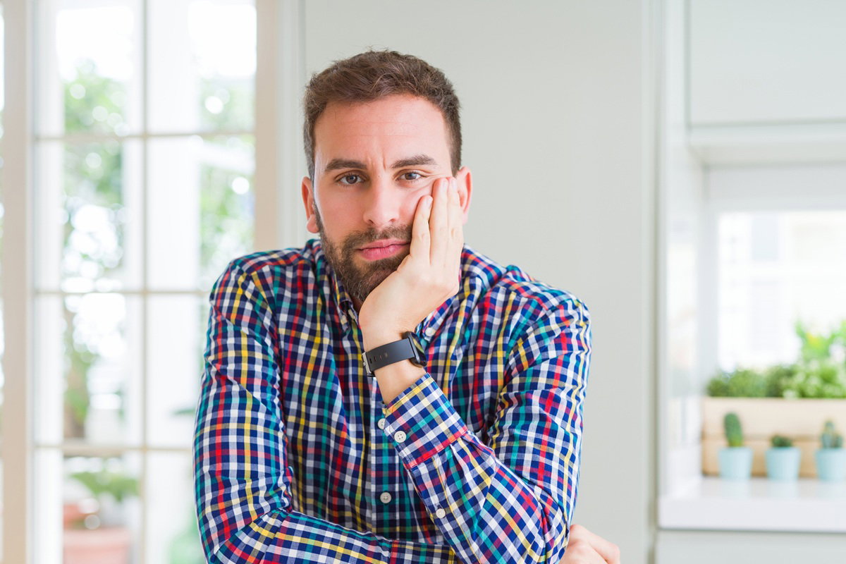 mężczyzna w wieku 35 plus w kracistej koszuli siediz zamyślony przy stole na tle okna