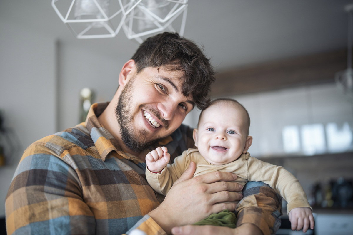 mężczyzna w wieku 30 plus z małym niemowlęciem na rękach uśmiechają się