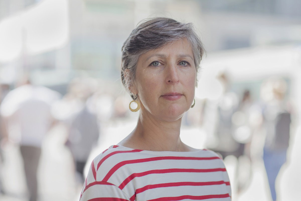 kobieta w dojrzałym wieku z krótkimi włosami kolczykami w i bluzce w paski stoi na ulicy ze smutną miną