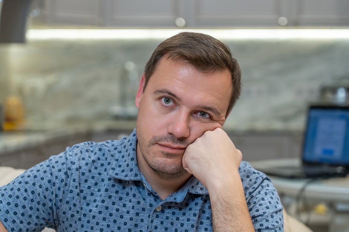 mężczyzna w wieku około 40 lat siedzi w kuchni zrezygnowany i zadziwiony