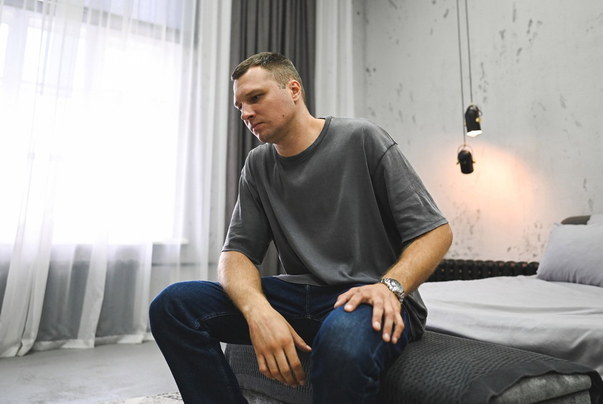 mężczyzna w wieku 30 lat w szarej koszulce siedzi na łóżku załamany i zamyślony