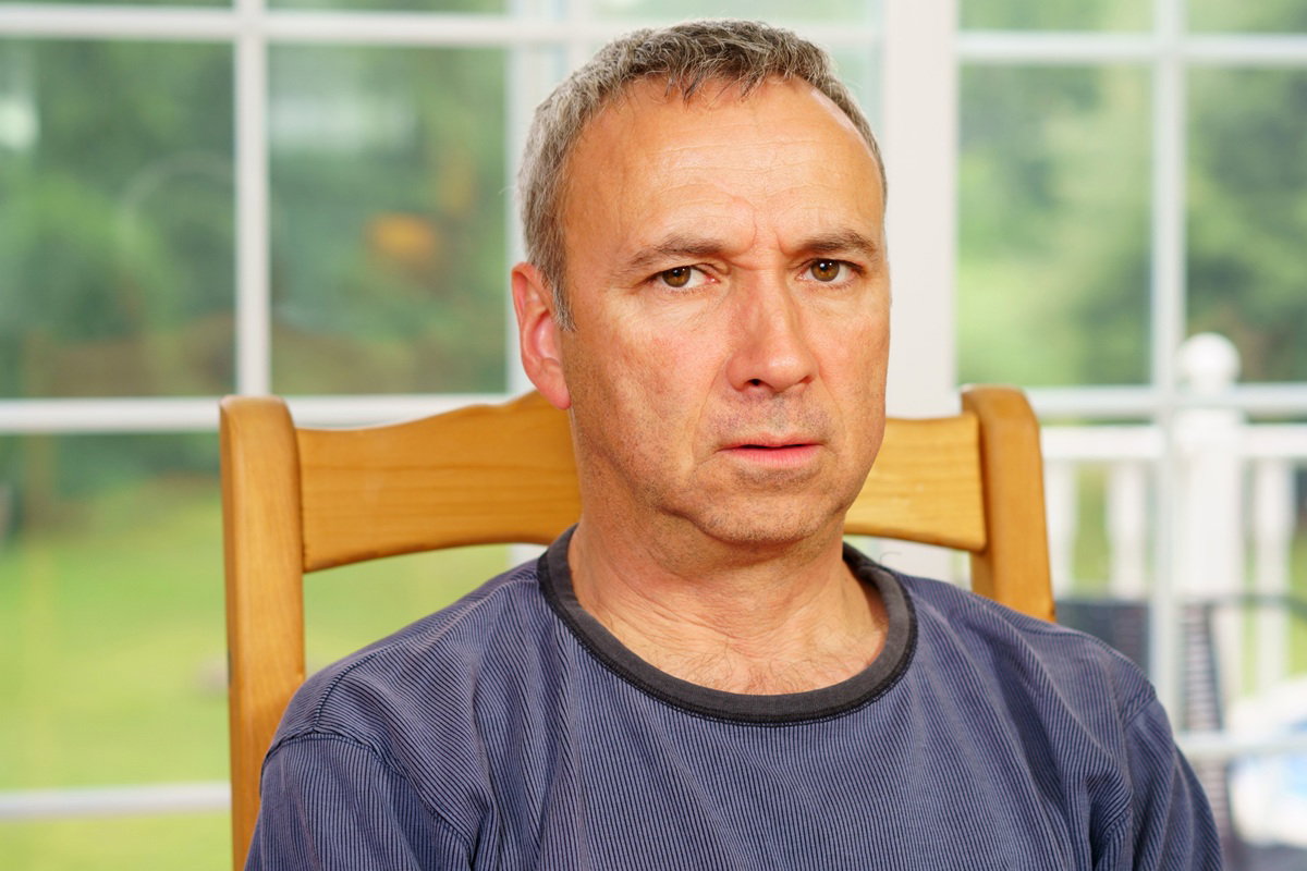 mężczyzna w wieku 40 plus siedzi na krześle na tle okna i jest zdegustowany