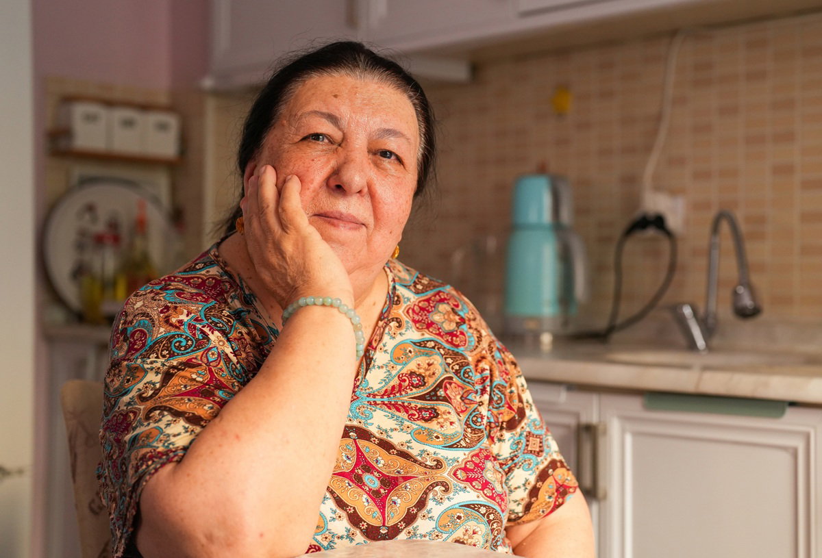 kobieta w wieku 65 plus we wzorzystej bluzce siedzi w kuchni zamyślona