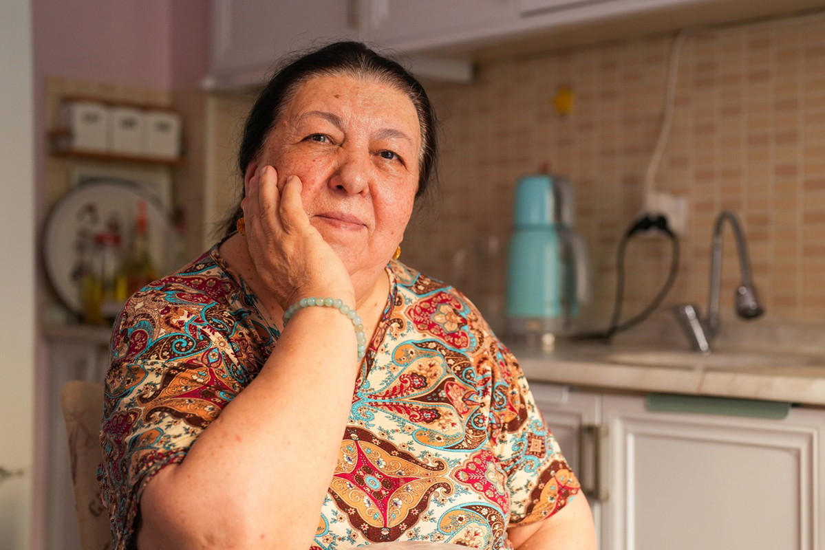 kobieta w wieku 65 plus we wzorzystej bluzce siedzi w kuchni zamyślona