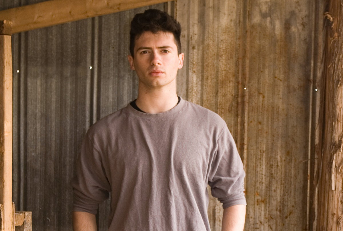 młody chłopak w wieku około 20 lat stoi na tle blaszanej ściany zamyślony i poważny