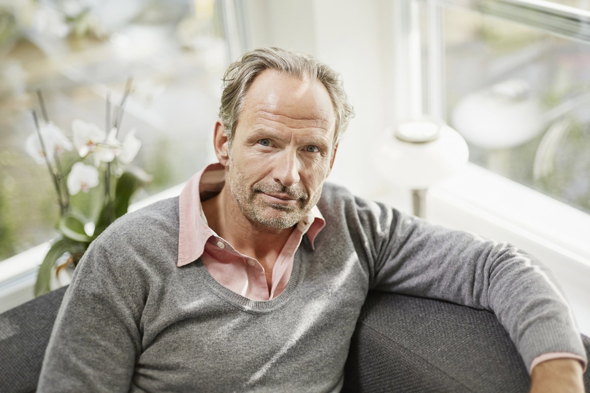 mężczyzna w wieku 45 plus łysiejący z zarostem siedzi i patrzy poważnym wzrokiem