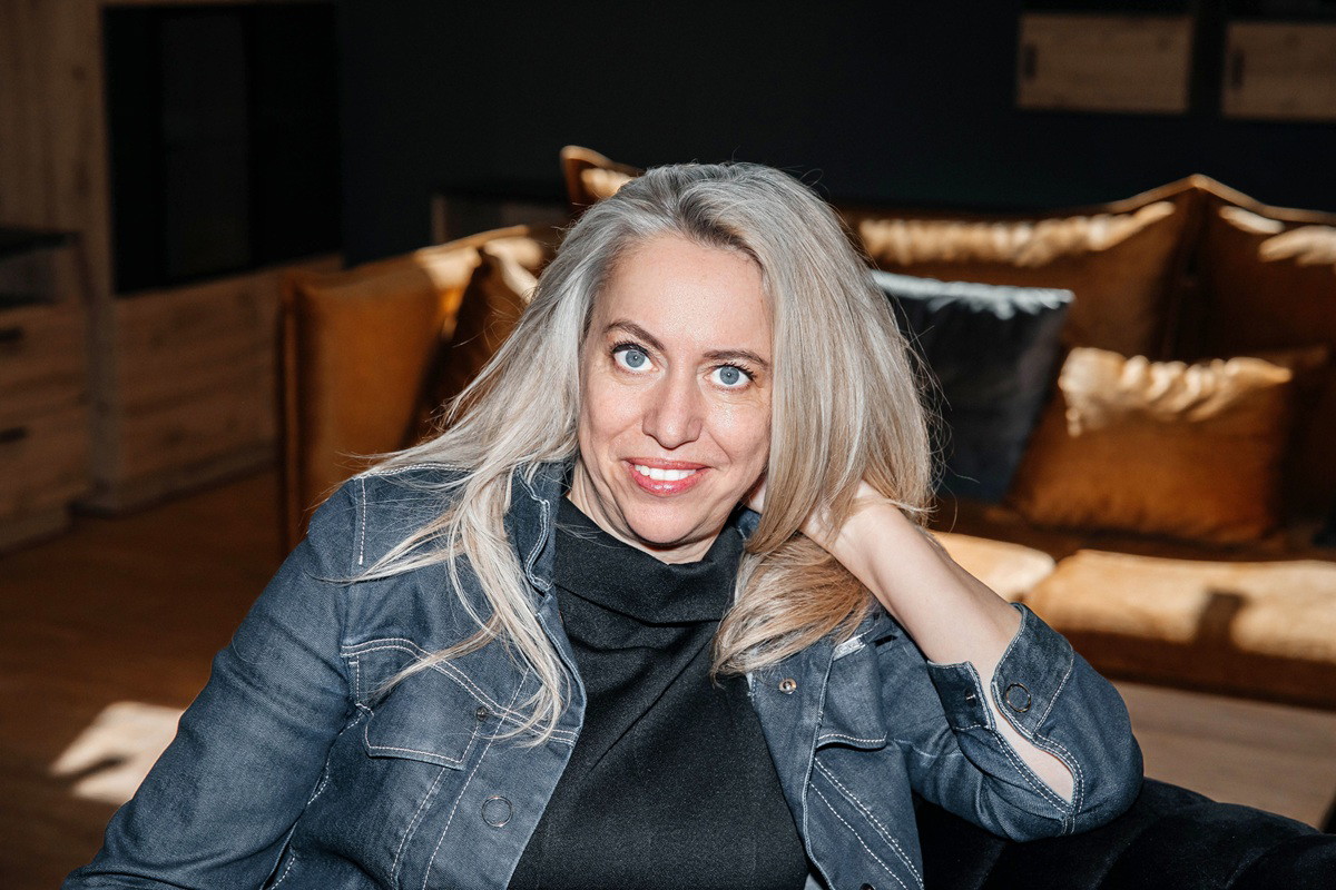 kobieta w wieku 40 plus blondynka z długimi włosami siedzi na kanapie z lekkim uśmiechem