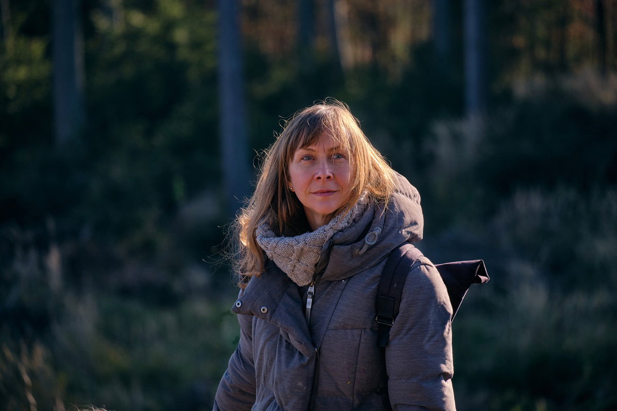 kobieta w wieku 40 plus w szarej kurtce stoi zamyślona na zewnątrz