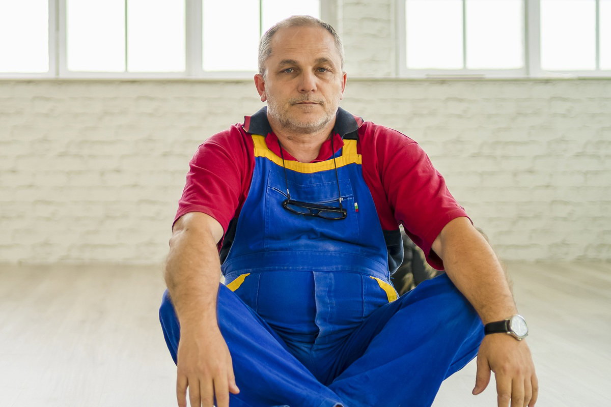 mężczyzna w wieku 50 plus siedzi na ziemi zrezygnowany w kombinezonie roboczym