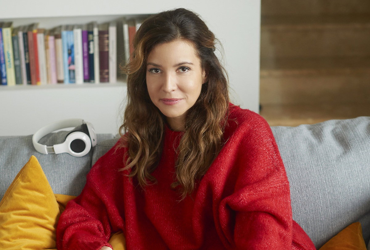 kobieta w wieku 30 plus w czerwonym swetrze siedzi na kanapie i lekko się uśmiecha rozmarzona