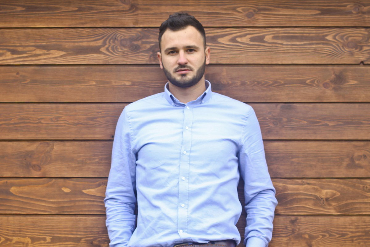 mężczyzna w wieku 35 plus stoi na tle drewnianej ściany zamyślony i smutny