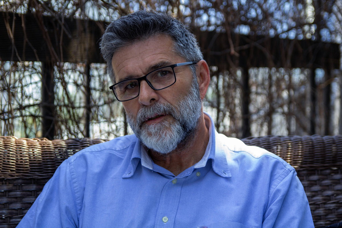 mężczyzna w wieku 60 lat siwiejący z zarostem i w okularach siedzi na zewnątrz zamyślony