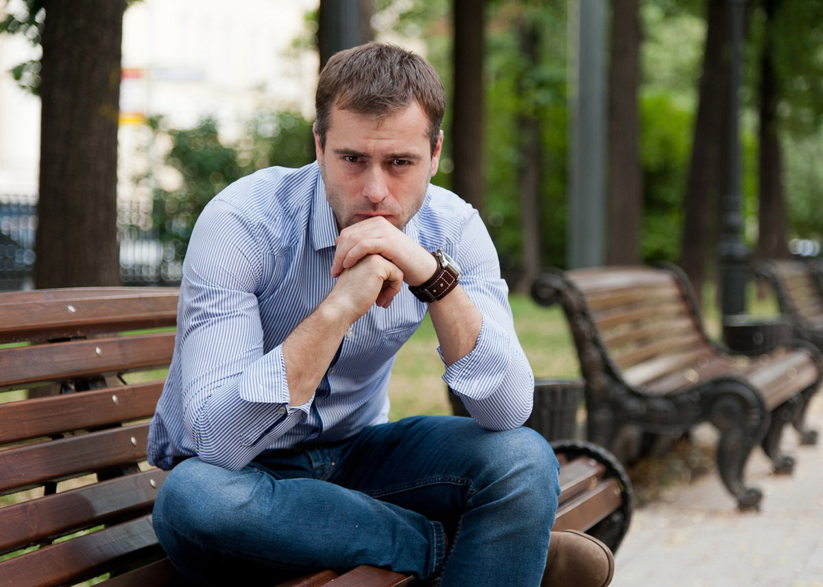 mężczyzna w wieku 35 plus w koszuli siedzi na ławce w parku zamyślony